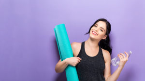 woman with yoga mat and water bottle against a purple background